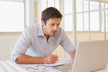 Fototapeta premium Businessman working on blueprints and laptop in office