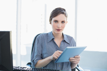 Lovely businesswoman using her tablet sitting at her desk