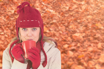 Happy blonde in winter clothes holding mug against autumn leaves on the ground