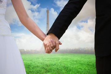 Mid section of newlywed couple holding hands in park against eiffel tower