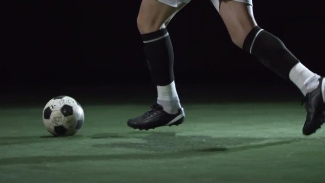 Male soccer player dribbling a ball on stadium field with artificial turf in low key lightning