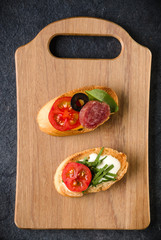 Open faced sandwich canape or crostini on a wooden serving board on dark stone  background closeup. Top view.