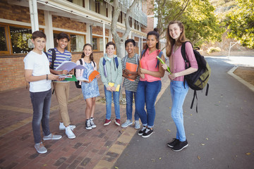Portrait of happy students standing with books on road