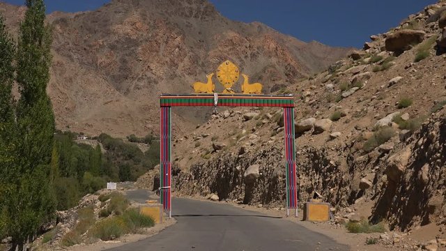 Gates of Likir Gompa Buddhist monastery decorated with Dharmachakra or wheel of Dharma flanked by pair of deers against picturesque rocky mountains and clear blue sky. Ladakh, India. Camera zooms out.