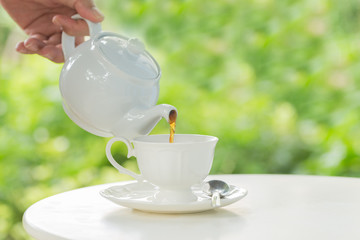 coffee pot pouring hot coffee into a cup during breakfast in morning sunlight