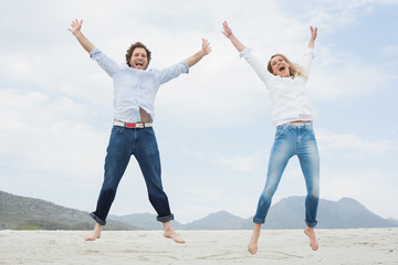 Fototapeta na wymiar Cheerful young couple jumping at beach