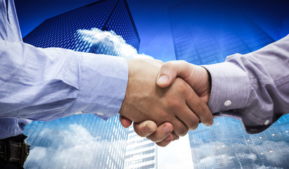 Two men shaking hands against low angle view of skyscrapers