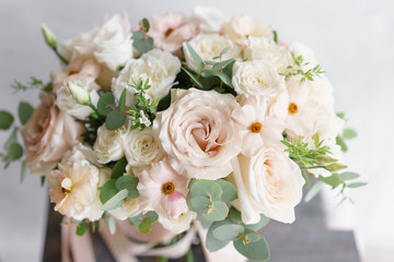 Wedding bouquet of white roses and buttercup on a wooden table. Lots of greenery, modern asymmetrical disheveled bridal bunch