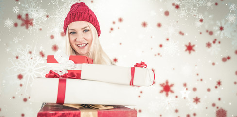 Festive blonde holding pile of gifts against snowflake pattern