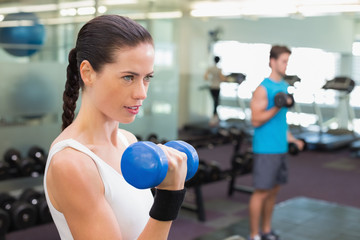 Fit brunette lifting blue dumbbell