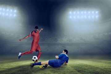 Obraz na płótnie Canvas Football players tackling for the ball against large football stadium under blue sky