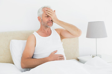 Thoughtful mature man sitting in bed