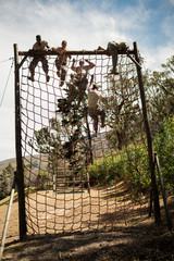 Military soldiers climbing rope during obstacle course