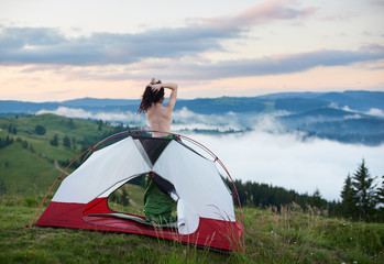 Back view of sporty naked woman traveller standing in tent entrance, enjoying beautiful view of...