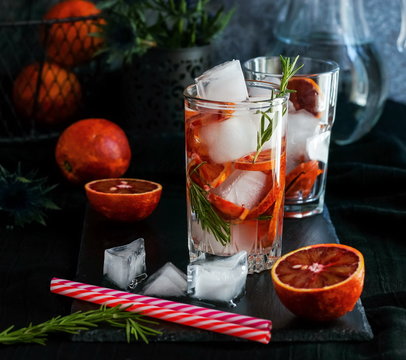 Detox water, refreshing cocktail with red blood orange, ice and rosemary on dark background.