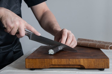 Process of making maki sushi. Cook chef hands preparing rolls with cheese, avocado, salmon and sesame seeds on wooden board 