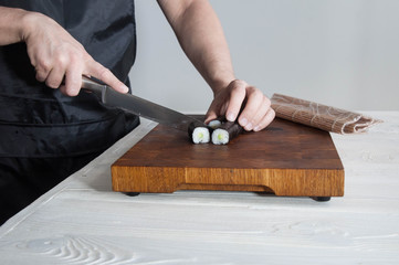 Process of making maki sushi. Cook chef hands preparing rolls with cheese, avocado, salmon and sesame seeds on wooden board 