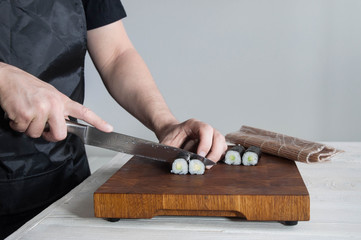 Process of making maki sushi. Cook chef hands preparing rolls with cheese, avocado, salmon and sesame seeds on wooden board 