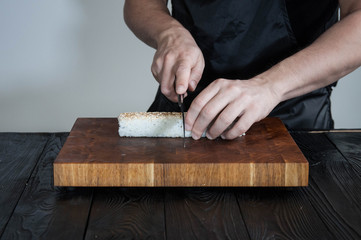 Process of making maki sushi. Cook chef hands preparing rolls with cheese, avocado, salmon and sesame seeds on wooden board 