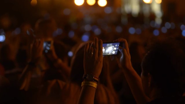 Person in the crowd making video and photos with fireworks on the smartphone. Concept: people, festival, crowd, firework, night, beauty, technology
