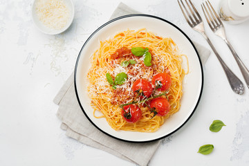 Traditional Italian dish of spaghetti with tomato sauce and parmesan cheese in ceramic plate on light concrete background. Selective focus. Top view.