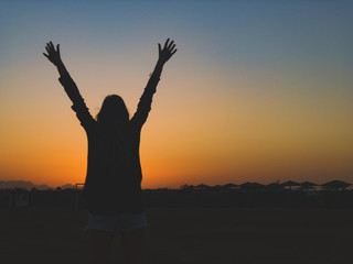 Silhouette of a girl with arms wide open in sunrise / sunset time.