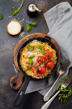 Traditional Italian dish of spaghetti with tomato sauce and parmesan cheese in iron frying pan on dark old concrete background. Selective focus. Top view.