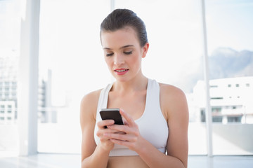 Concentrated fit brown haired model in sportswear using her mobile phone