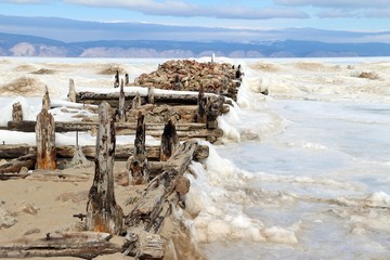 Remainder of wooden jetty in front of old fish factory on Olkhon island, Irkutsk, Russia. Surrounded by ice of Baikal lake in late winter.