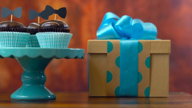 Happy Father's Day close up of woman arranging and setting up gift, cupcakes and card against rustic wood background.