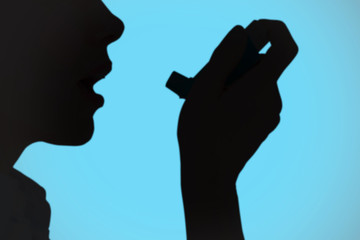 Close up of a woman using an asthma inhaler against blue background with vignette