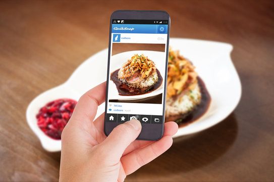 Female hand holding a smartphone against delicious duck breast dish with rice and chutney