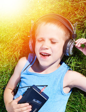 Little boy lying on grass with old audio cassette player