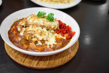 Delicious Japanese hamburg curry Serve with and mozzarella cheese on top with Rice, curry Rice in white plate on a black table with copy space.   