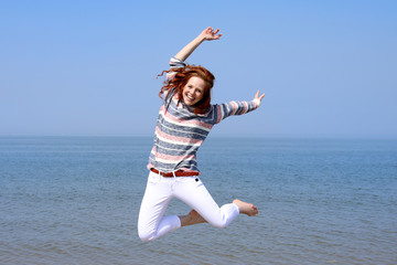Hübsche rothaarige Frau an einem Strand springt in die Luft und Meer im Hintergrund
