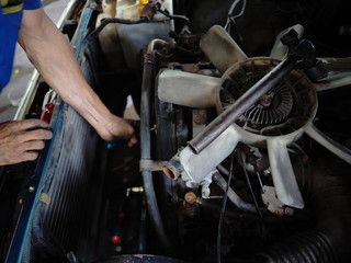 Old cooling fan motor of car is being removed in garage. Auto repair service.