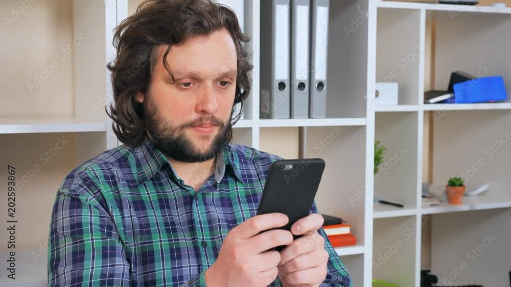 Poster handsome man sitting at the workplace using smartphone. smiling businessman chatting online or texti