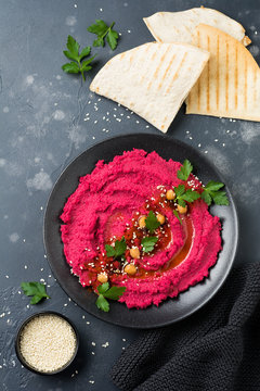 Homemade beetroot hummus in black ceramic dish on old dark concrete background. Selective focus. Top view.