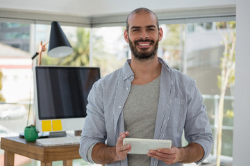 Portrait of smiling designer using digital tablet while standing in office