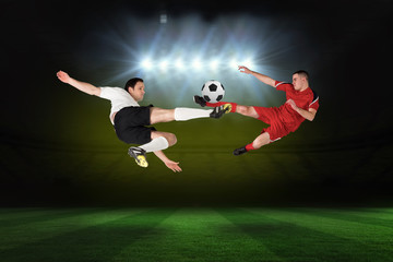 Obraz na płótnie Canvas Football players tackling for the ball against football pitch under spotlights