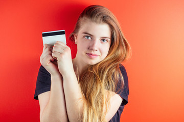 young and beautiful teenage girl with beautiful blond long hair is holding a credit card near the face on an orange wall background. credit card, business, debt, credit, online purchase, shopping