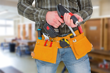 Manual worker holding gloves and hammer power drill  against workshop