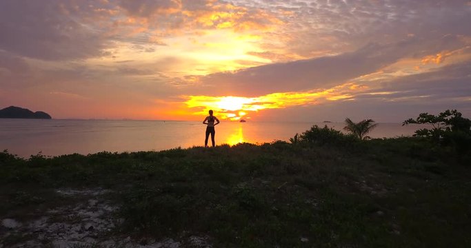 Fly cam hold running athlete woman jogging at top on the sunset beach line and raises his hands to meet the sun.Tracking shot with the opening of the panorama to the sea and empty sky