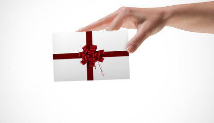 Female hand showing a card against red christmas bow and ribbon