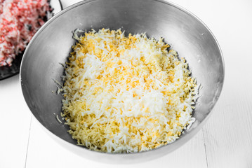 Salad preparation: finely chopped surimi crab sticks, eggs, cheese and mayonnaise in a metal bowl on a white table