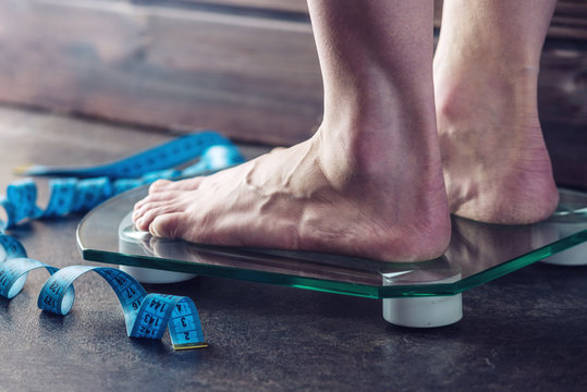 Female feet standing on electronic scales for weight control on dark background. Concept of sports training, diets