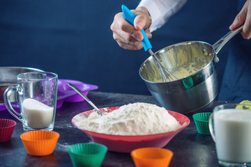 Chef pastry in a black apron in the process of making cupcakes from ingredients. Concept of confectionery cooking