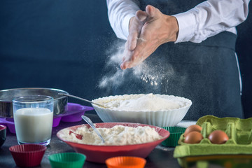 Chef pastry in a black apron in the process of making cupcakes from ingredients. Concept of confectionery cooking