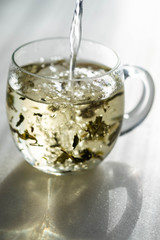 Tea pouring into glass cup isolated in white.