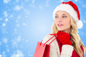 Happy festive blonde with shopping bag against white snowflake design on blue